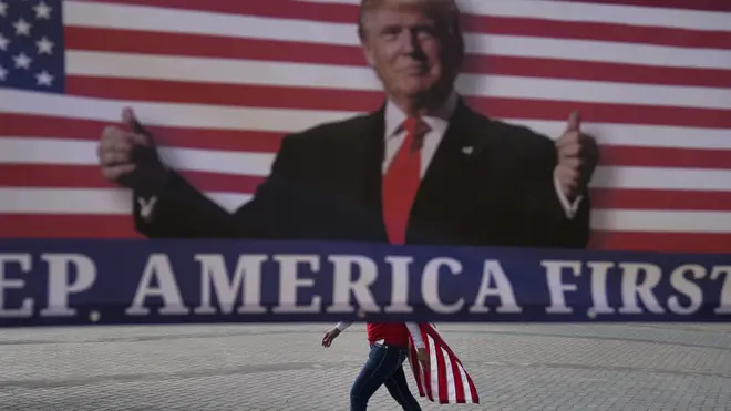 A woman draped in an American flag walks past a banner supporting President Donald Trump (Jae C. Hong/AP)