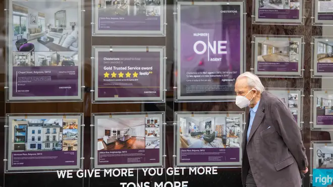 A man wearing a protective face mask passes an estate agents' window in Knightsbridge, London