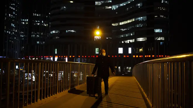 A man wearing a face mask to protect against the spread of the coronavirus wheels a suitcase across a pedestrian bridge in Beijing (Maek Schiefelbein/AP)