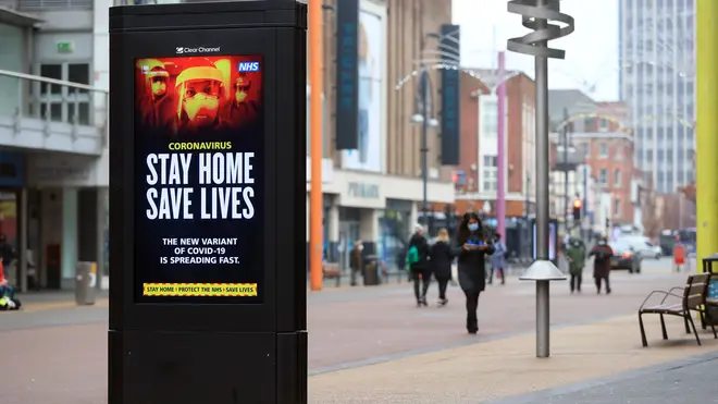 People pass a Stay Home, Save Lives electronic board