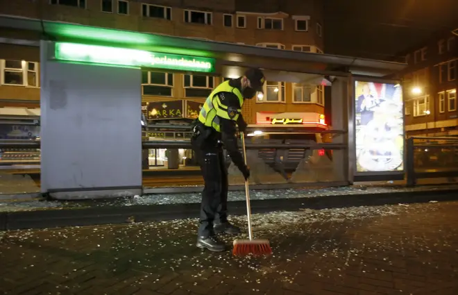 A police officer sweeps up glass from a bus stop that was smashed in protests against a nation-wide curfew in Rotterdam