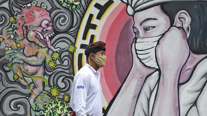 A man walks past a coronavirus-themed mural in Bali, Indonesia