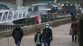 People wearing masks walk by the Thames in central London