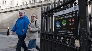 People wearing plastic visors walk past a coronavirus prevention poster in the City of London as England remains under third lockdown