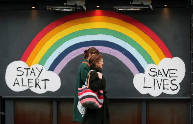 Two women walk past a graffiti with the message 'Stay alert, save lives' in London