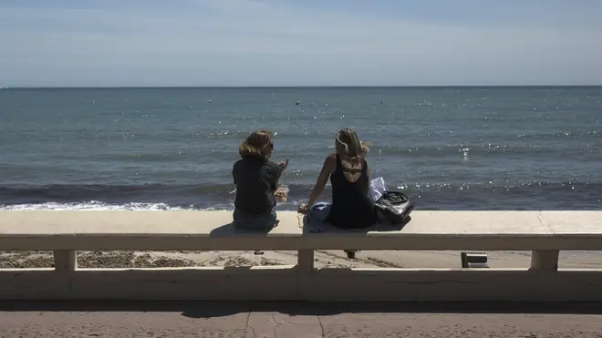 Two women sit above a deserted beach in Cannes