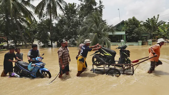 People push belongings through a flooded area in Indonesia
