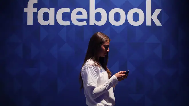 File photo of a woman using her phone under a Facebook logo