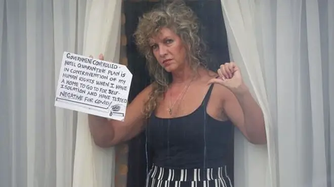 A quarantined traveller holds a sign up to the window of her room.