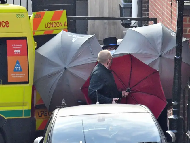 Staff and police hid the occupant of an ambulance using umbrellas amidst a larger police presence.