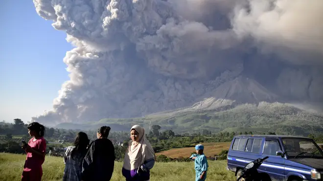 People stand and look at the erupting Indonesian volcano
