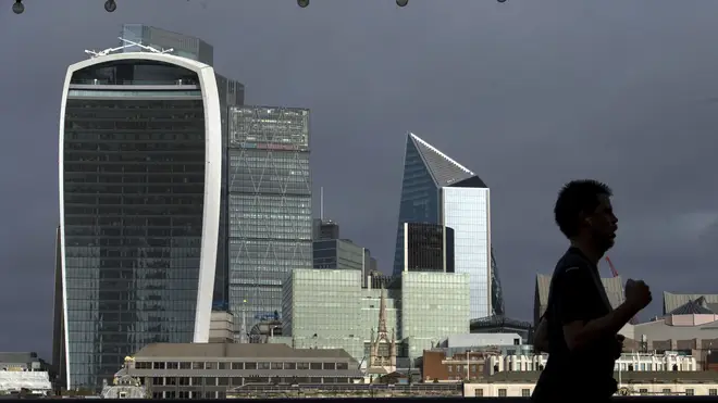 A person jogs along the riverside path past the City of London skyline