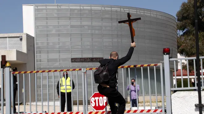 A protestor holding a cross climbs a gate outside Cyprus’s national broadcasting building