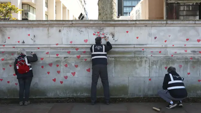 Members of bereaved families paint red hearts on the COVID-19 Memorial Wall opposite the Houses of Parliament at Embankment
