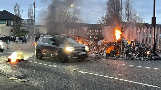 A car drives past a bus that was set on fire amid disorder in Northern Ireland