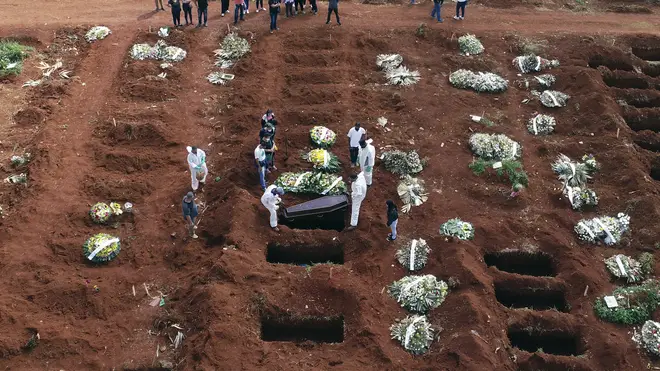 Cemetery workers wearing protective gear lower the coffin of a person who died from complications related to Covid-19 into a gravesite in Brazil