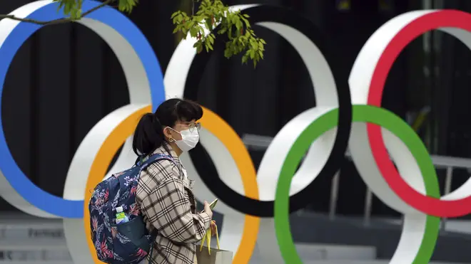 A woman wearing a protective mask walks in front of the Olympic Rings in Tokyo