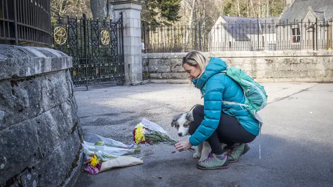 A woman, with dog, lays flowers at the gates of Balmoral Castle in Royal Deeside