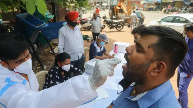 A healthcare worker collects a mouth swab sample from a man at a road side testing centre in New Delhi