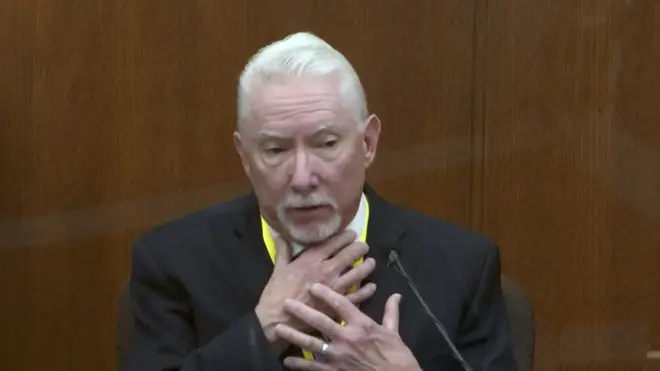 Barry Brodd testifies while placing his right hand across his own throat