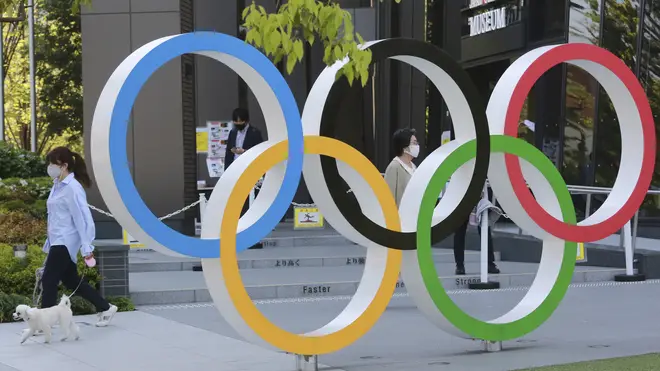 A woman with her dog walks past the Olympic rings in Tokyo