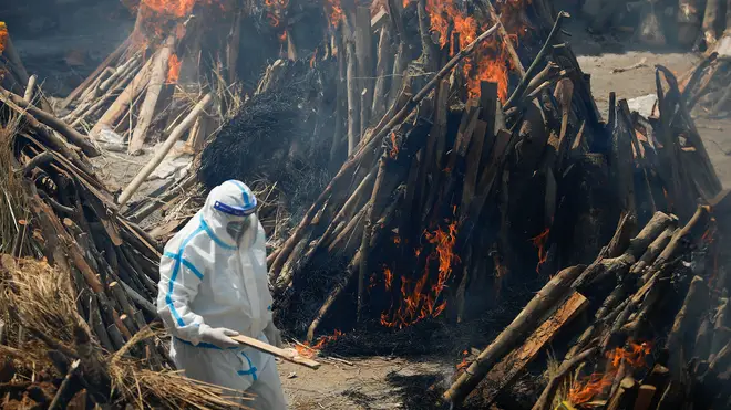 A man wearing PPE walks through burning pyres of people who have died from Covid-19