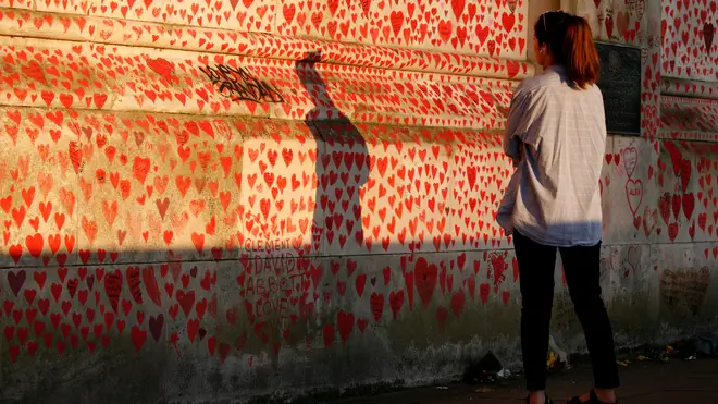 A woman looks at the National Covid Memorial Wall of hearts, each heart representing an individual coronavirus death, in evening sunlight in London
