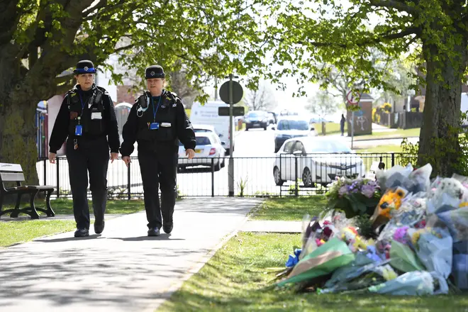 Police Community Support Officers walk past floral tributes in a park close to where the body of PCSO Julia James was found.