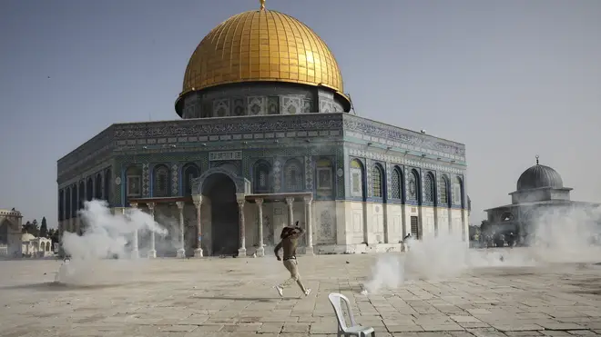A Palestinian man runs away from tear gas during clashes with Israeli security forces in front of the Dome of the Rock Mosque at the Al Aqsa Mosque compound in Jerusalem’s Old City