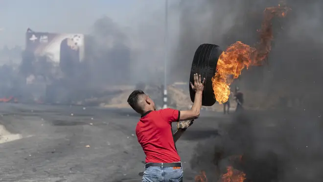 A Palestinian protester rolls a burning tyre towards Israeli army soldiers during clashes at the northern entrance of the West Bank city of Ramallah