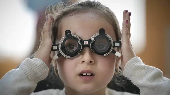 A little girl adjusts testing glasses during an eyesight examination (Vadim Ghirda/AP)