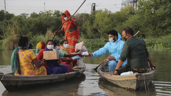 Indian man Himanshu, wearing personal protective suit as a precaution against the coronavirus distributes free aid procured by him to people living in a small island in River Yamuna in New Delhi, India (Amit Sharma/AP)