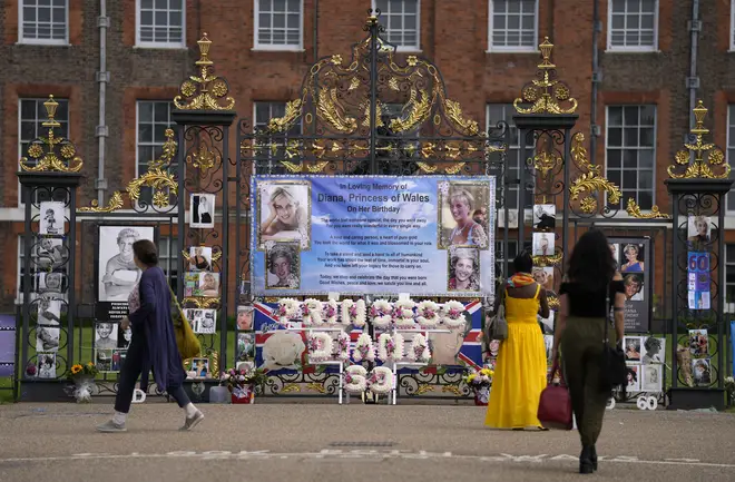 People look at tributes placed on the gates of Kensington Palace in London
