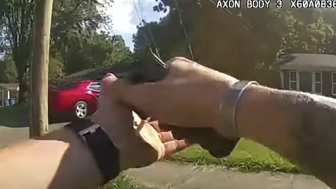 An officer is seen approaching a red car with his sidearm raised