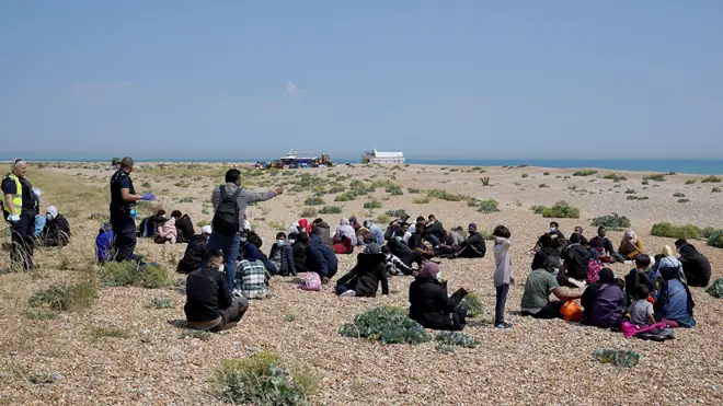Migrants sit on the beach after arriving on a small boat at Dungeness in Kent