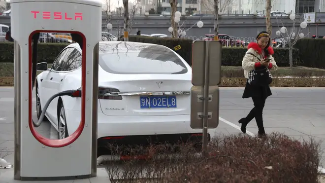 A woman walks past a Tesla car being charged in Beijing