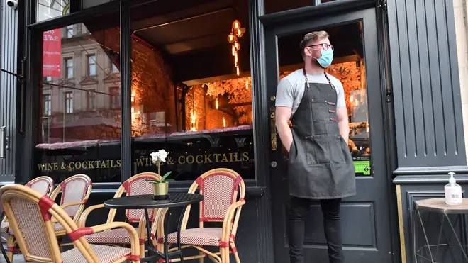 A bartender wearing a face mask stands outside a bar in Cardiff