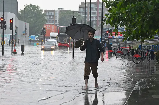A pedestrian walks bare-footed along a flooded road in The Nine Elms district of London