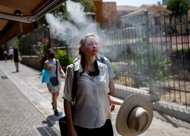 A tourist walks through a mist of water sprayed outside a café in Athens