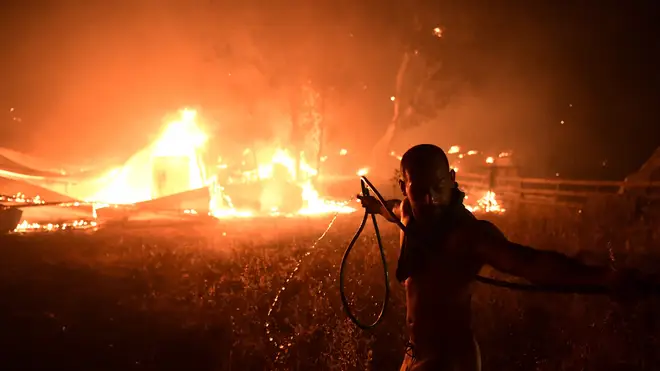 A man uses a water hose during a wildfire in northern Athens