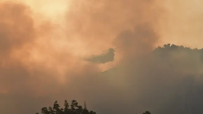 An aircraft drops water during a wildfire in ancient Olympia