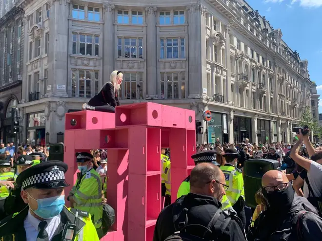 A protester with Extinction Rebellion climbing on top of a pink box in Oxford Circus.