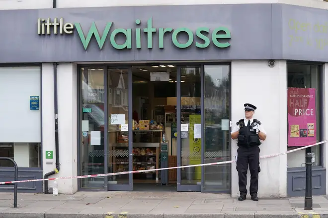 A police officer stands outside Little Waitrose on Fulham Palace Roa