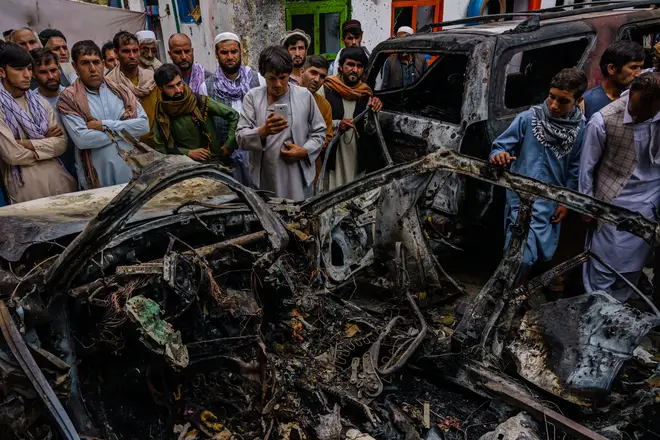 Relatives and neighbours of the Ahmadi family gather round the remains of a car that was hit by a US drone strike, reportedly killing 10 members of the family