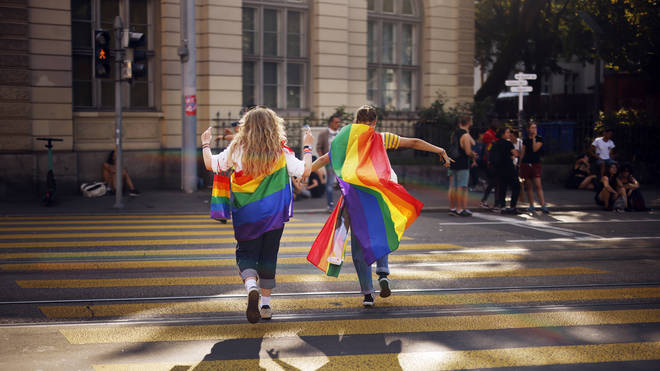 Two people cross a road draped in rainbow coloured flags