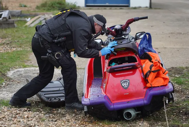 A police officer inspects the boat after it was brought ashore in Dungeness.