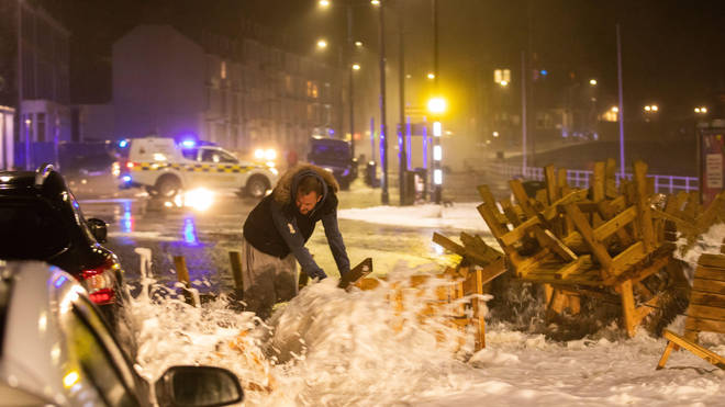 A person tries to clear the road as Storm Barra creates huge waves in Aberystwyth