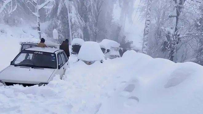 People walk past vehicles trapped in heavy snow in Murree