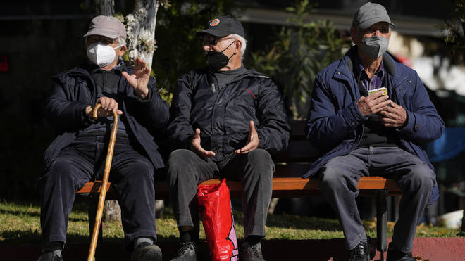 Three elderly men wearing FFP2 face masks to curb the spread of coronavirus sit on a bench in Athens, Greece