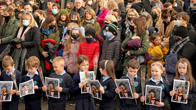 Pupils from Ashling Murphy's class hold photographs of her and red roses outside St Brigid's Church.